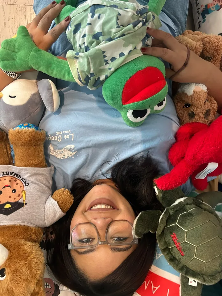 Steph lying on the floor surrounded by soft toys, smiling up at the camera